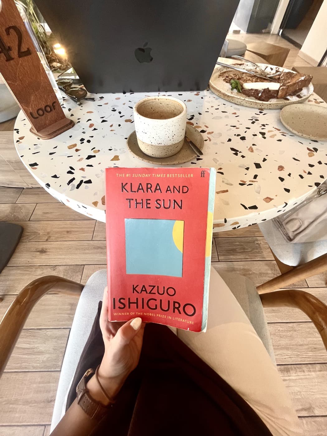 Holding Kazuo Ishiguro's Klara and the Sun at a cafe table next to a coffee