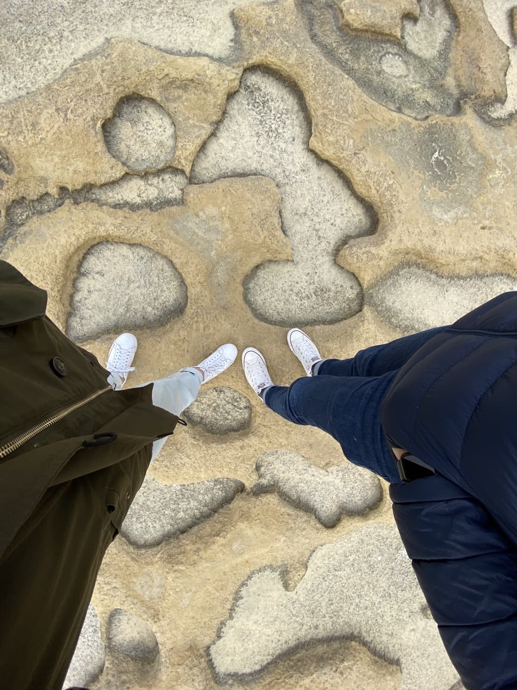 Two pairs of white trainers side by side on weathered, pitted rock